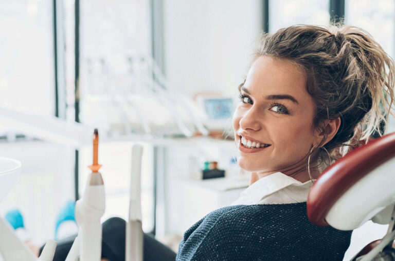 A woman smiling at the camera while sitting in a dental chair for a dental exam.