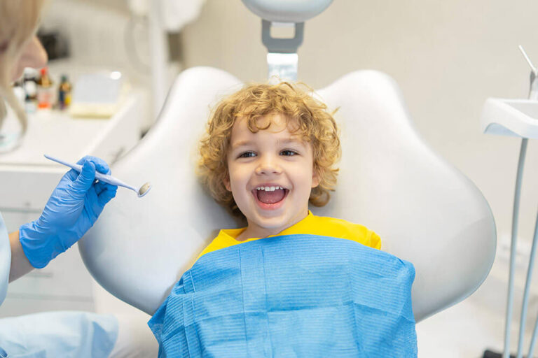 A young boy with curly blonde hair smiling as he prepares for his pediatric dental appointment.